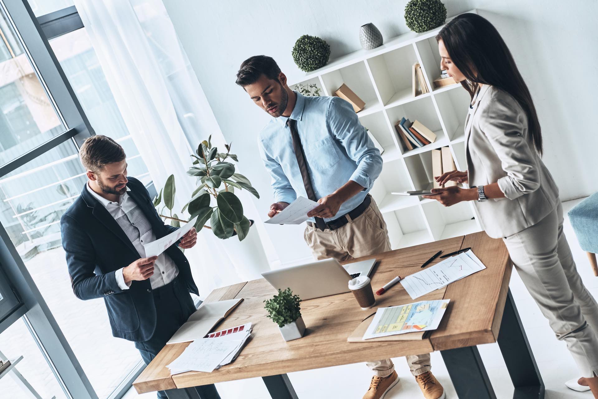 Successful business team. Top view of young modern people in smart casual wear discussing business while standing in the creative office Successful business team. Top view of young modern people in smart casual wear discussing business while standing in the creative office