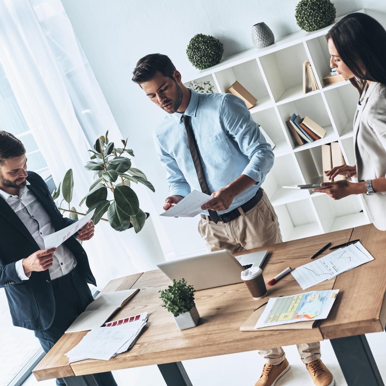 Successful business team. Top view of young modern people in smart casual wear discussing business while standing in the creative office Successful business team. Top view of young modern people in smart casual wear discussing business while standing in the creative office
